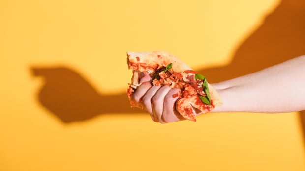 DP pizza SMUSHED Partial view of woman squeezing piece of pizza in hand on yellow background - null